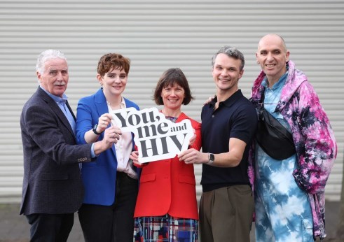 Group of 5 people standing in a line. Together they are holding a sign that reads 'You, Me and HIV'