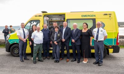 Large group of people, including National Ambulance Service staff standing in front of an ambulance.