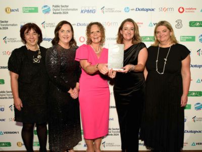 Five women standing indoors, two in the centre are holding a plaque.