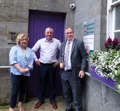 A woman and two men Waterford are standing outside a blue door. The sign next to the door reads: Substance Misuse Service. 