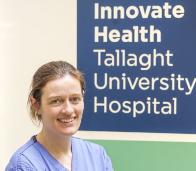 Dr Aoife Doolan looking straight ahead. Behind her is a large sign that reads: Innovate Health Tallaght University Hospital