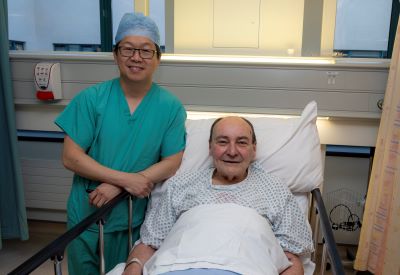 A doctor wearing green scrubs is standing next to a male patient in a hospital bed.