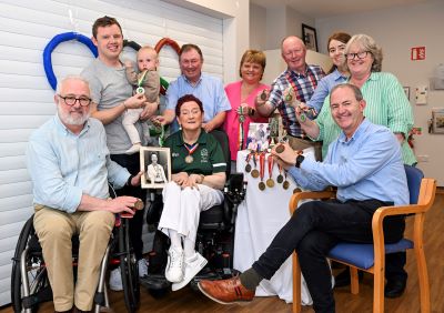 Large group of family, some seated, some standing. They are all gathered around Monica O’Kelly with her Paralympic medals.