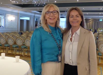 2 smiling women standing together in a large hotel function room. 