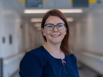 A woman smiling and standing in the corridor of a clinical setting.