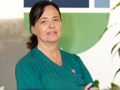 A woman standing indoors wearing green medical scrubs.