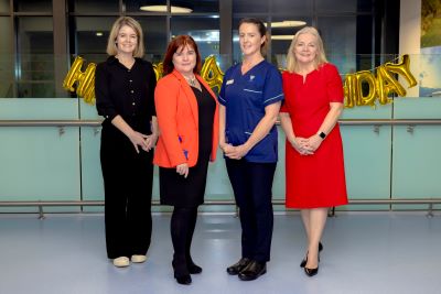 4 women standing in a line in front of a balloon banner. They are in a healthcare setting. One of the staff in wearing a healthcare uniform. 