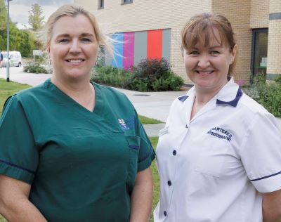 Two female healthcare workers standing side by side outside a healthcare building. 