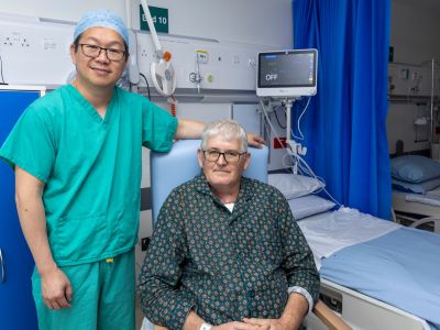 A clinical healthcare worker standing beside an older patient sitting in a clinical setting.