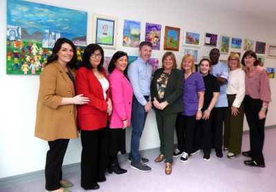 Large group of people standing in a corridor in front of a selection of colourful paintings on a wall.