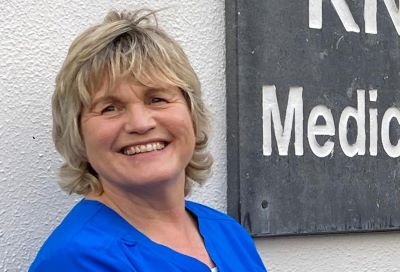 Orla Loftus is wearing a blue healthcare worker tunic. She is smiling.