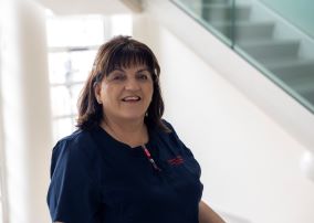 A smiling woman in a blue healthcare worker tunic 