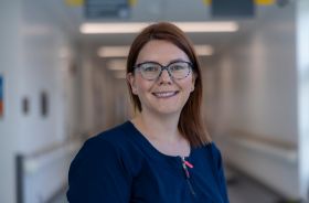 A woman smiling and standing in the corridor of a clinical setting.