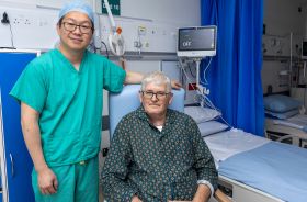 A clinical healthcare worker standing beside an older patient sitting in a clinical setting.