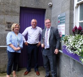 A woman and two men Waterford are standing outside a blue door. The sign next to the door reads: Substance Misuse Service.