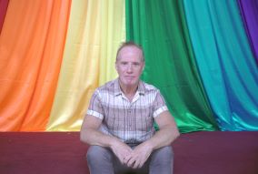 Will is seated in front of a rainbow background